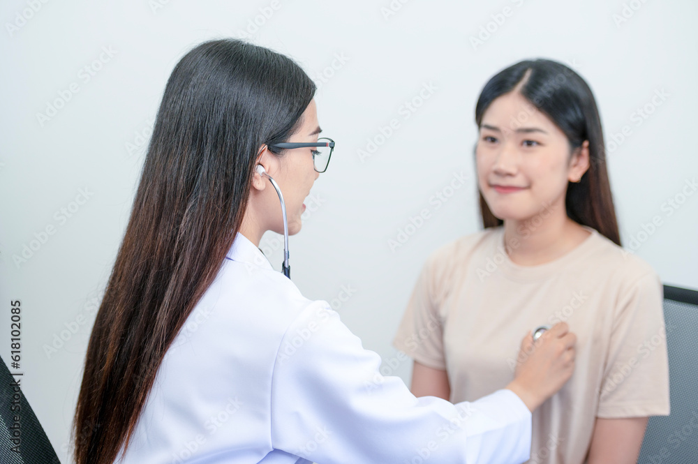 Asian female doctor in uniform holding a stethoscope and using it to measure the heart rate of an asian female patient with heart disease Asian female doctor in uniform holding a stethoscope and using it to measure the heart rate of an asian female patient with heart disease