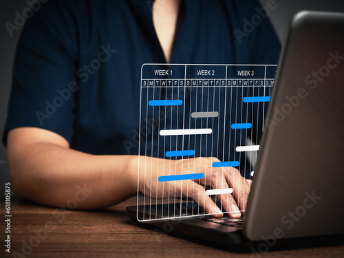 Project manager working on a laptop and updating tasks and milestones progress planning with a Gantt chart scheduling interface on a virtual screen.