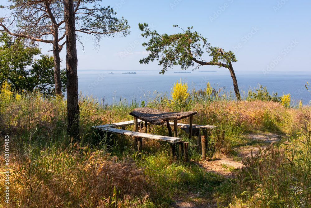 Old wooden table and benches in the countryside with grass and trees on the shore of a large lake or reservoir on a sunny summer day Old wooden table and benches in the countryside with grass and trees on the shore of a large lake or reservoir on a sunny summer day