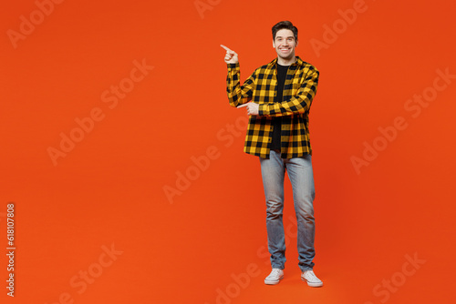 Full body young caucasian man wear yellow checkered shirt black t-shirt point index finger aside indicate on workspace area copy space mock up isolated on plain red orange background studio portrait.