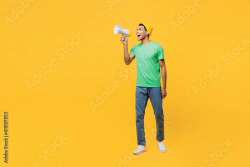 Full body young man of African American ethnicity he wears casual clothes green t-shirt hat hold in hand megaphone scream announces discounts sale Hurry up isolated on plain yellow background studio. © ViDi Studio