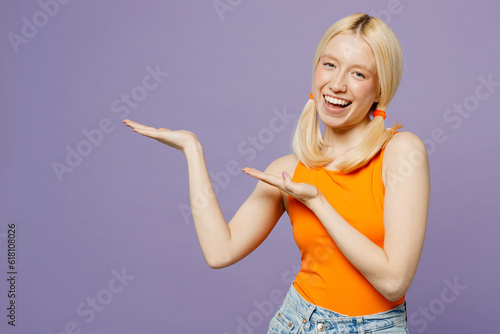 Young blonde woman she wear orange tank shirt casual clothes point arms hands aside indicate on workspace area copy space mock up isolated on plain pastel light purple background. Lifestyle concept.