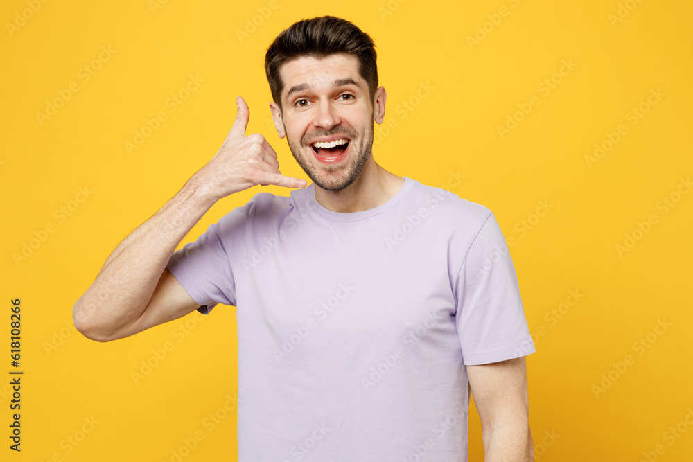 Young cheerful happy smiling caucasian man he wear light purple t-shirt casual clothes do phone gesture like says call me back isolated on plain yellow background studio portrait. Lifestyle concept Young cheerful happy smiling caucasian man he wear light purple t-shirt casual clothes do phone gesture like says call me back isolated on plain yellow background studio portrait. Lifestyle concept