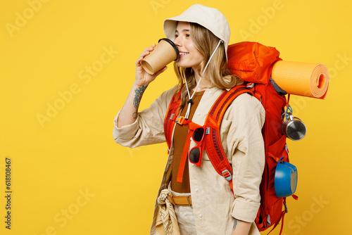 Young woman carry backpack with stuff mat holding takeaway cup coffee to go isolated on plain yellow background Tourist leads active lifestyle walk on spare time. Hiking trek rest travel trip concept