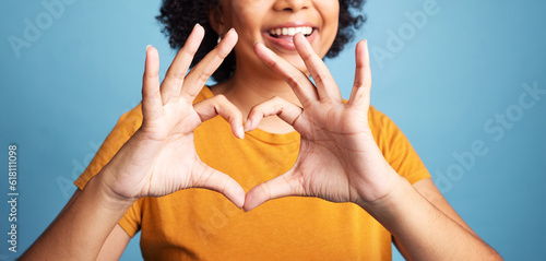 Happy, hand and closeup of a heart shape for romance, care or flirting expression in a studio. Happiness, positive and zoom of a woman with a love gesture, emoji or sign isolated by a blue background