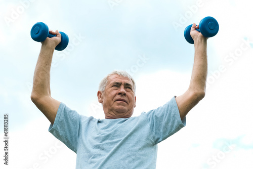 Senior man working out outdoor. Person lifting dumbbells. Old male exercising against blue sky. Healthy people lifestyle. Active sport training. Older elderly sportsman doing fitness exercise. Workout