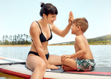 Lake, mother and son on paddle board, high five and relax outdoor, summer holiday and travel. Adventure, freedom and fun, family with woman and boy child in swimsuit, vacation and bonding together