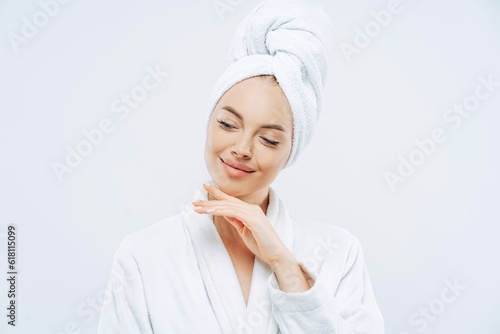 Natural woman touches jawline, towel on head, dries hair, cares for body, clean skin, prepares for party photo