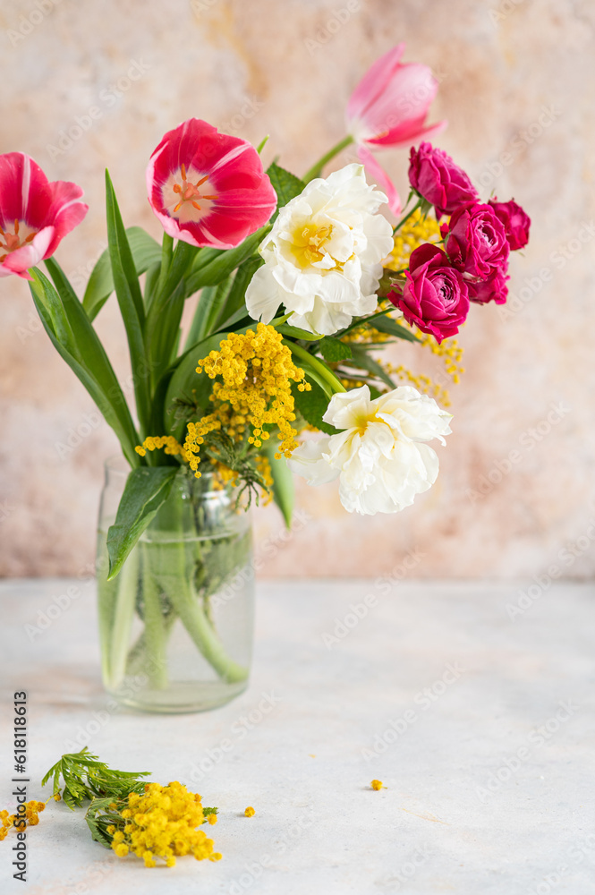 Obraz premium Glass vase with bouquet of beautiful tulips and mimosa in the light background