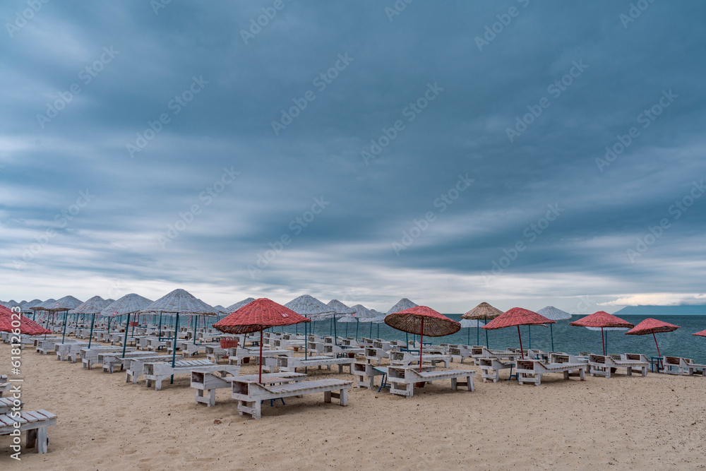 Sun bed chairs with matress and straw beach umbrellas on beach. Blue hour time background by the sea..
