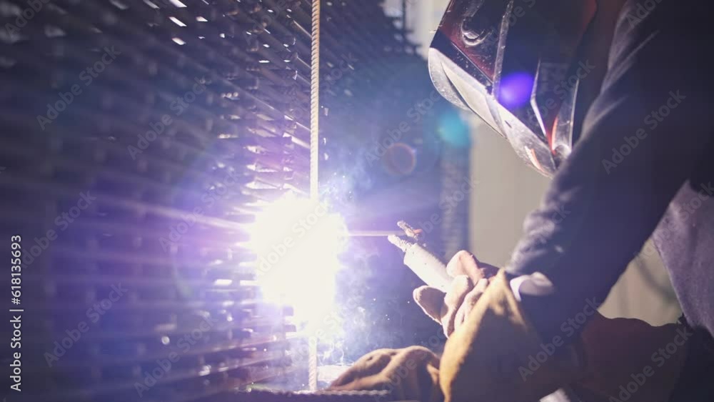 A welder at a construction site welds metal. Sparks and smoke from electric welding. A welder at a construction site welds metal. Sparks and smoke from electric welding.