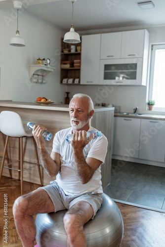 Senior man siting on fit ball doing exercise with two bottle of waters insted of dumbbell  during the day. photo