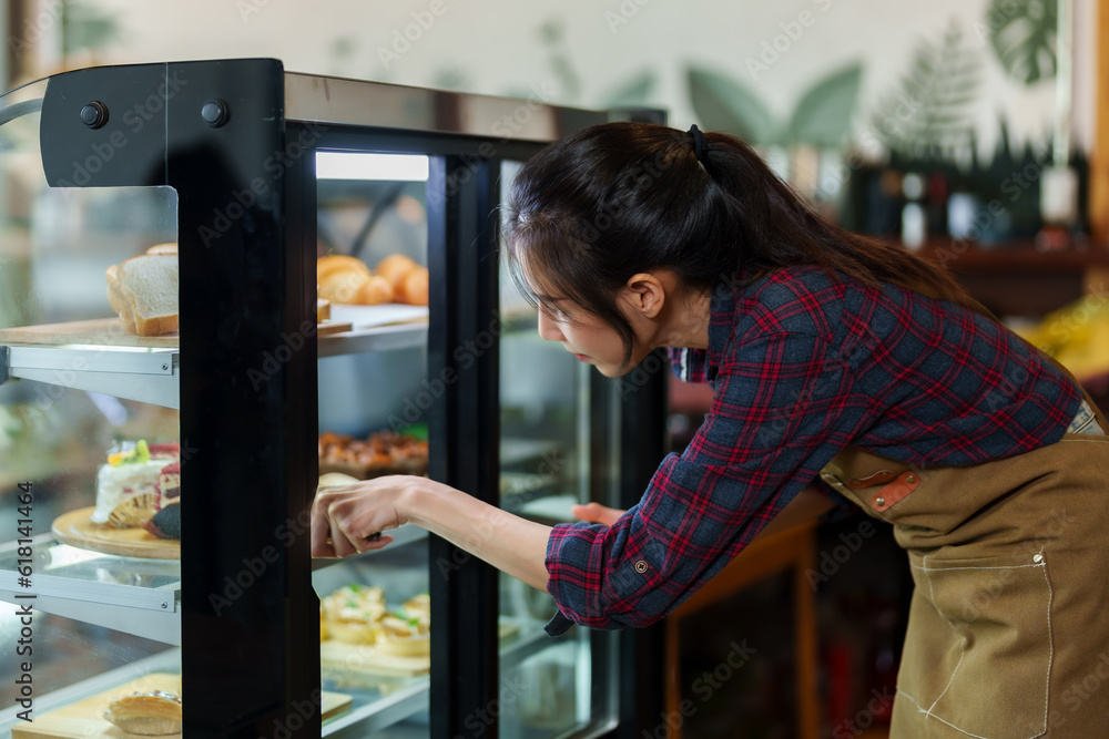 Close-up, cafe worker is opening bakery cabinet, bent down use tongs pick cake in refrigerator out put them on sall tray, that is served customers who order eat in store, close cabinet when finished.