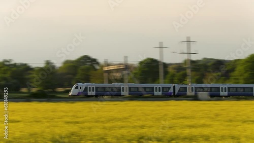 Panning shot of a train passing a field of oilseed rape yellow flowers in the British or English countryside at dusk
