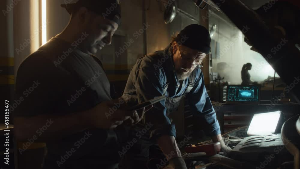 Mature Caucasian and young Middle Eastern men working in auto service garage checking functionality of car motor Mature Caucasian and young Middle Eastern men working in auto service garage checking functionality of car motor
