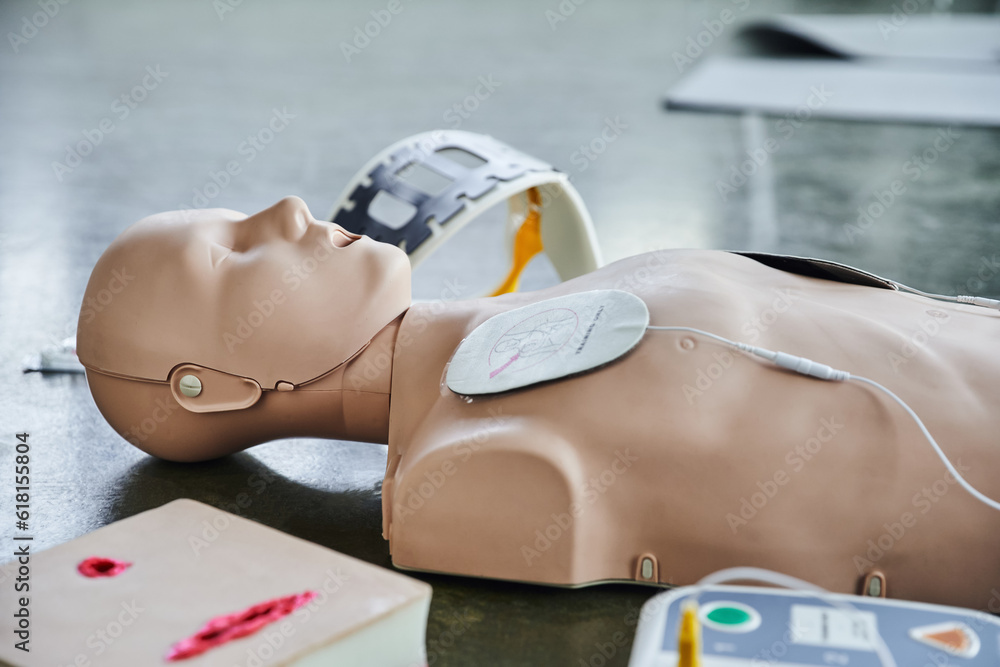 CPR manikin near automated external defibrillator, wound care simulator and neck brace on