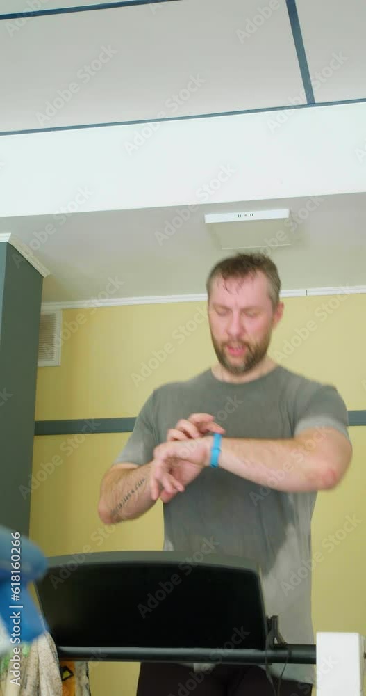 Slow motion vertical video of a middle-aged man monitoring his heart rate with his smartwatch while exercising on a treadmill. A smart approach to training using modern technology.