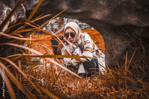 Girl wearing hijab sitting and frowning on the other side of the rock © vnllstrwbrry