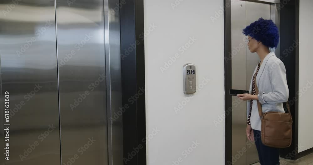 Biracial businesswoman with blue afro using smartphone and entering elevator in office, slow motion Biracial businesswoman with blue afro using smartphone and entering elevator in office, slow motion