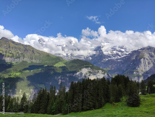 A view on the Berner Oberland, Switzerland. Mountain peaks, clouds, blue sky, sunny day. Forest in the montains. Pines. Alps, alpine rocks, remaining snow, ice. Glacier. Jungfrau region.