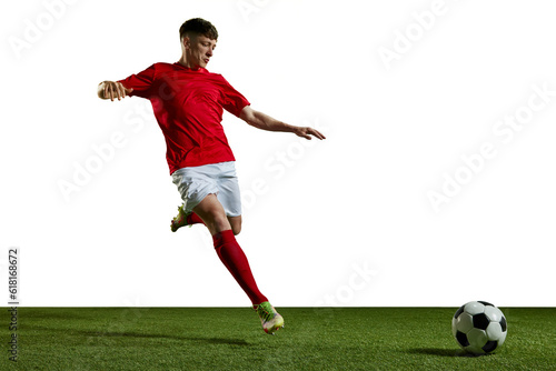 Young man in red uniform, football player in motion, playing, kicking ball on sports field against white background. Concept of professional sport, action, lifestyle, competition, hobby, training, ad © master1305