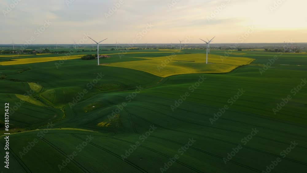Windmill farm with rotating blades in agronomic field at sunset. Electricity, ecological saving and alternative power source Windmill farm with rotating blades in agronomic field at sunset. Electricity, ecological saving and alternative power source