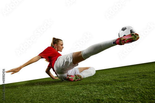 Motivated female athlete, young girl, football player kicking ball in motion on field grass against white background. Concept of professional sport, action, lifestyle, competition, hobby, training, ad