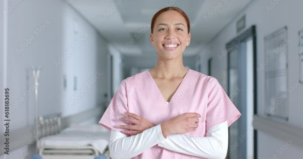 Portrait of happy biracial female doctor wearing scrubs, smiling in corridor, slow motion Portrait of happy biracial female doctor wearing scrubs, smiling in corridor, slow motion