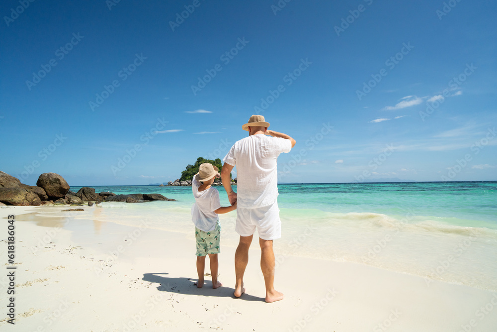 Father and son holding hands, having fun together, walking on the tropical beach. Fathers day. Summer vacation.