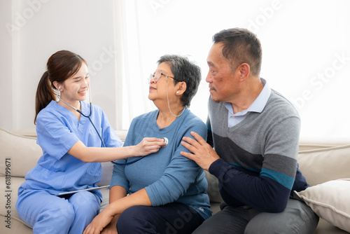 Asian senior patient talking with doctor and nurse on sofa at home