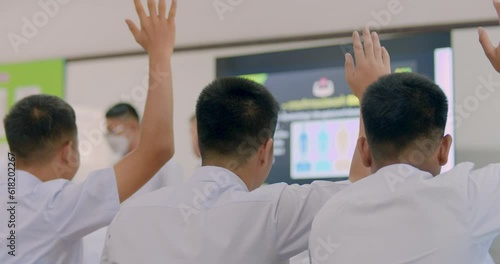 Slow motion of Asian high school students in white uniform actively study science by raising their hands to answer questions that teachers ask them by television in the classroom.