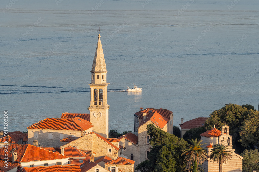 Long shot of the beautiful old town of Budva with the picturesque houses and the tower surrounded by the calm waters of the Adriatic Sea in the golden hour before sunset, Montenegro