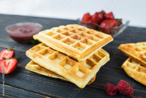 Square Belgian waffles with berries on a wooden background.