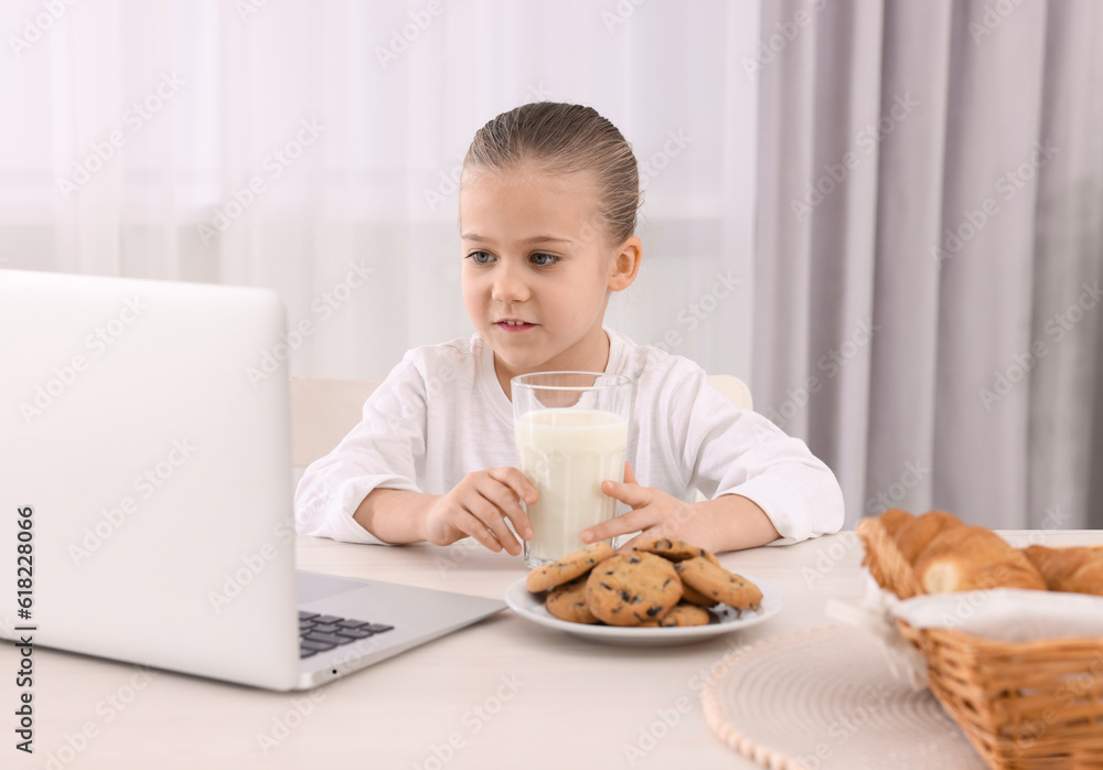 Little girl using laptop while having breakfast at table indoors. Internet addiction Little girl using laptop while having breakfast at table indoors. Internet addiction