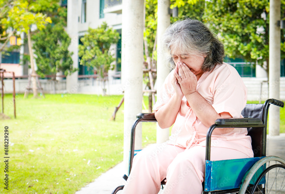 An elderly Asian female patient sits in a wheelchair in a hospital, she regrets her illness. Elderly disease concept, health insurance An elderly Asian female patient sits in a wheelchair in a hospital, she regrets her illness. Elderly disease concept, health insurance