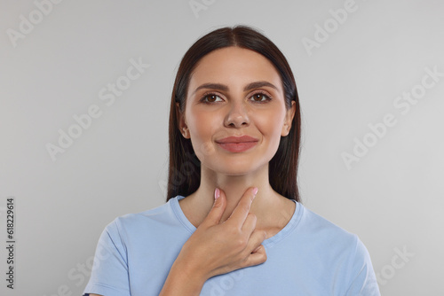 Endocrine system. Young woman doing thyroid self examination on light grey background