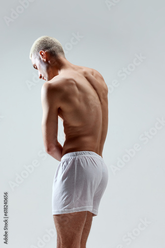 Strong, muscular, relief male back. Healthy body. Young handsome man posing in underwear against grey studio background. Concept of male natural beauty, body care, health, sport, fashion, ad photo