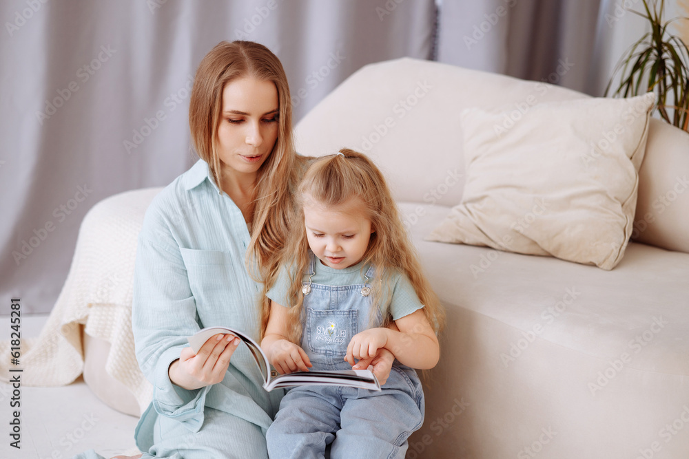 Mom and little daughter in blue pajamas are hugging in a beautiful and fabulous bedroom with lots of pink gypsophila flowers. The concept of happy childhood, children's health and motherhood. Mom and little daughter in blue pajamas are hugging in a beautiful and fabulous bedroom with lots of pink gypsophila flowers. The concept of happy childhood, children's health and motherhood.