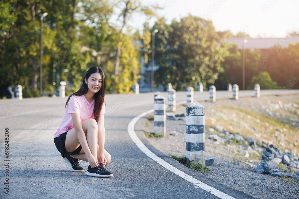 Female runner kneeling and tying shoelace on the street. Fitness woman tying shoelaces. Young woman runner tying shoelaces in park with sunset and sunbeam.