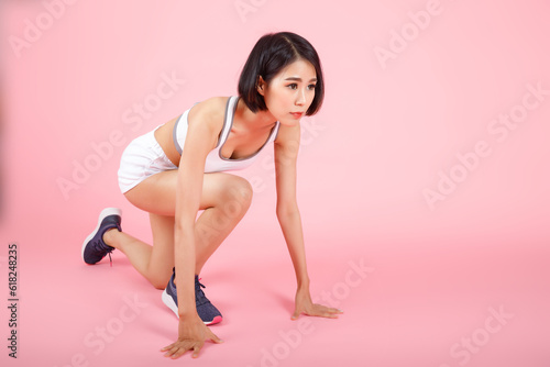 Sporty young woman in crouch start position isolated on pink background. Female Athlete Runner. Confident young female athlete in starting position ready to start a sprint.