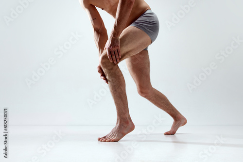 Knee pain. Cropped image of male legs against grey studio background. Model in underwear holding knee, suffering from pain. Concept of male natural beauty, body care, health, sport, fashion, ad