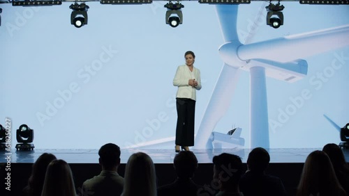 Caucasian woman female speaker presenting on the stage during ecological renewable energy conference. Future technology meetup. Talks about green energy sources, wind turbines, solar power photo