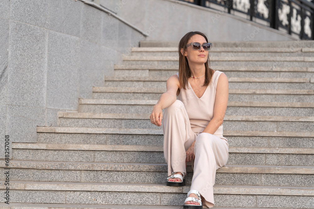 Summer urban portrait of a young woman who sits on the steps in the street. Summer urban portrait of a young woman who sits on the steps in the street.