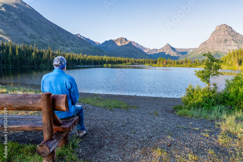 Man, person sitting watching a scene of a lake surrounded by trees and a rugged mountain in the background, Pray Lake, Two Medicine Area, Glacier National Park, Montana photo