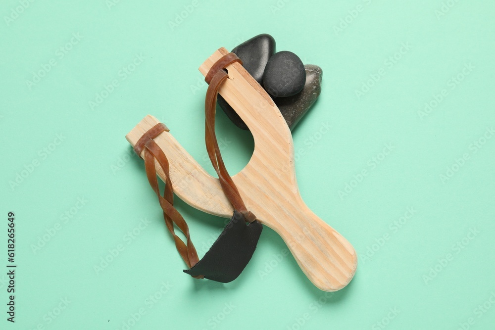 Wooden slingshot with stones on light green background, top view Wooden slingshot with stones on light green background, top view