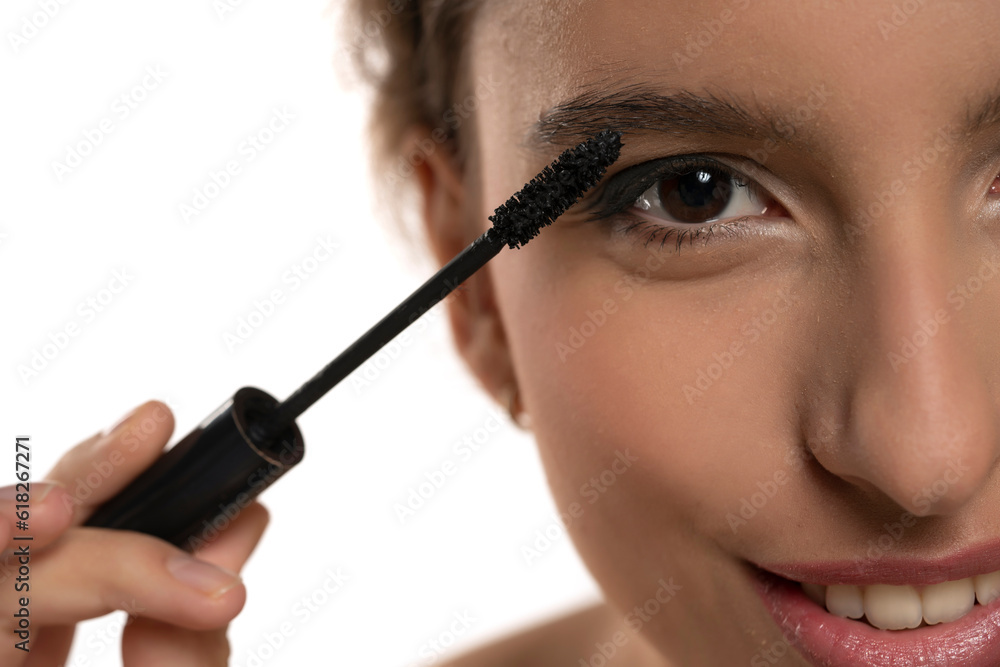 closeup of a young smiling woman applying mascara on a white background