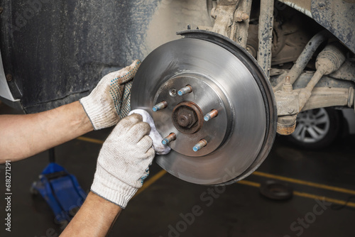 An auto mechanic removes dirt and grease residue from a newly installed car brake disc with a tissue