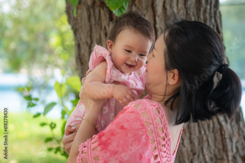 Asian mum and little child - young happy and beautiful Chinese woman playing on city park with adorable and cheerful baby girl in mother and daughter love and bonding