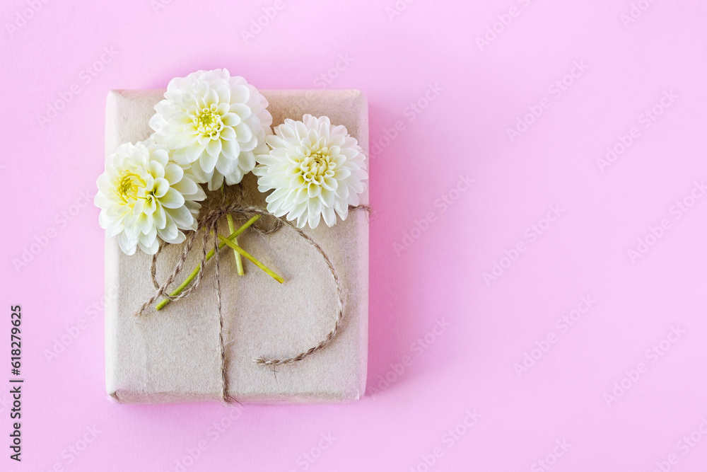 Gift box in gray craft paper decorated with white dahlia flowers on a pink background for the holiday. Gift box in gray craft paper decorated with white dahlia flowers on a pink background for the holiday.