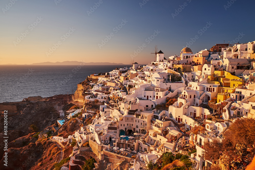 Beautiful view from the old castle of Oia village with traditional white houses and windmills in Santorini island in Aegean sea at sunset, Greece